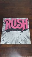 Front cover of Rush self-titled vinyl record showing large pink 'RUSH' logo with artistic black and white background.
