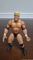 Front view of WWE Psycho Sid action figure showing muscular build, blond hair, black trunks, boots, elbow pads, and white wristbands.