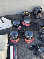 Black Franklin MLB batting helmets, catcher's helmets with face masks, Wilson chest protector and leg guards, Franklin pitching rubber/base, and baseball bat arranged on pavement.