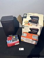 Photo of trash can, WD TV Live box, Gibson Bostwick BBQ grill box, and Joseph Joseph microwave pasta cooker box on black surface