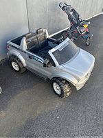 Silver Ford F150 Power Wheels electric ride-on truck from angled front left side with visible driver seats, wheels, and open bed