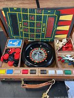Open box with roulette wheel, red and black chips, and white and red chess pieces along with numbered felt layout