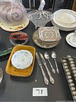 Overview of dishes, small plates, silver spoons, orange vase, and floral patterned plates