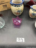 Two ceramic jars with blue rims and floral patterns surrounding a pink glass star-shaped candle holder on a table with a cardboard box partially visible.