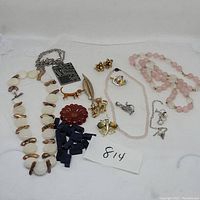 Photo of assorted jewelry laid out on white background including necklaces, pins, earrings, and beads with lot number card 814.