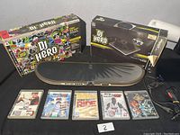 Wide shot of the DJ Hero turntable and box, along with five PlayStation 3 game cases laid out on a table.