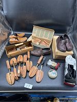 Overview of men's shoes, shoe stretchers, shoe care products including polish and measuring tape, displayed on black surface with some in boxes.