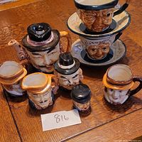 Group photo showing all Toby ceramic items including teapot, two cups with saucers stacked, creamer, sugar bowl, two mugs, and shaker with detailed face designs.
