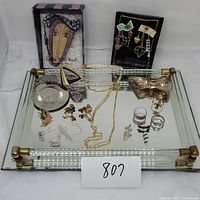 Overview of mirrored vanity tray displaying assorted jewelry including boxed Silvestri earrings, chain necklaces, rings, and other items.