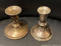 Front view of two antique silver weighted candlesticks on black surface showing tarnish and wear.