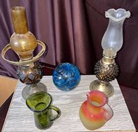 Full lot view showing all five glass items: two oil lamps, blue decorative glass ball, and two small pitchers.