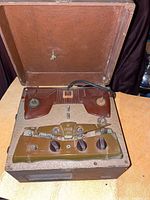 Open antique Ampro reel to reel tape player showing wooden hinged case, two tape spindles, and front control panel with knobs and switches.