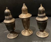Photo showing three antique sterling silver salt and pepper shakers standing upright against a dark background.