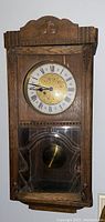 Front view of antique walnut pendulum wall clock showing carved wood details and round clock face with Roman numerals and brass center.
