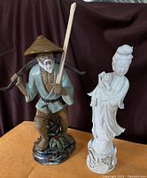 Photo showing two Asian ceramic figures side by side on a table with a dark backdrop.