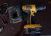 DeWalt cordless screwdriver drill with battery installed photographed alongside the matching battery charger on a dark surface.