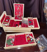 Full view of the open wooden jewelry box filled with assorted vintage costume jewelry including necklaces, pendants, bracelets, and earrings with red felt lining visible inside compartments.