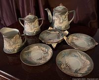 Full view of set with teapot, sugar bowl, creamer, and four saucers on dark wooden surface.