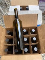 Top-down view of one box showing 12 amber glass bottles with cork tops, some bottles partially visible inside cardboard dividers.