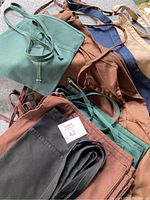 Image showing a pile of various aprons in green, brown, blue, beige, and black colors on a surface.