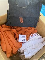 Box containing dark denim aprons, bright orange aprons, and white aprons stacked together.