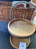Two-tiered wooden and metal dessert stand placed next to the wicker basket with faux food items inside, showing wood wear and metal handle.