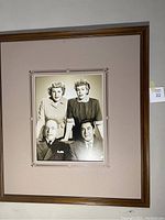 Black and white photo with 2 men seated and 2 women standing behind, in a vintage style, framed with wide beige mat and brown frame