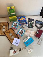 Overview of lot items arranged on table including two wood light switch covers, boxed John Deere matchbox holder, Hot Wheels Mustang car package, metal plaques, small book and other assorted items.