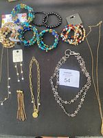 Overview of lot with multiple beaded bracelets, two necklaces, and one earring displayed on black surface.