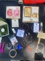 Full view of all costume jewelry items arranged on black surface including vintage Rolfs case and lighter, various earrings, bracelet and watch.