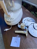 Full view of Cuisinart Custom Prep 11 food processor with motor base, two metal disc blades, plastic S-shaped chopping blade, and a white plastic attachment handle, placed on wooden surface with power cord visible.