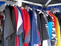 Photo of assortment of hanging men's cycling shirts and jerseys in various colors including black, red, blue, gray, and patterned designs.