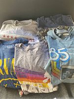 Six folded graphic t-shirts in various colors and designs placed in a box