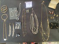 Overview of jewelry lot showing multiple necklaces, bracelets, and earrings arranged on a black surface.