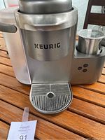 Front view of Keurig K-Cafe K84 coffee pod maker showing the logo, body and milk frother attachment.