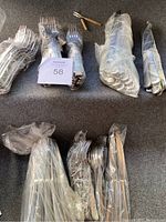 Overview of assorted forks, knives, and spoons laid out, mostly wrapped in plastic.