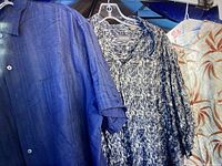 Two men's button-up shirts hanging on hangers: one solid blue and one black and white abstract pattern.