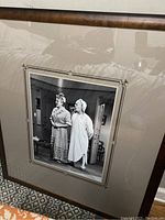 Photo of framed black and white movie still showing two women in period costumes on a stage or set.