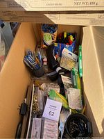 Box showing contents including pens, dry erase markers, tape, scissors, brass fasteners, and other office supplies.