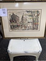 Framed watercolor painting of a Paris street scene with buildings, trees, pedestrians, and a domed church or monument in the background.