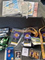 Photo shows stacked sealed PSA sports magazines, several Lakers lanyards with attached ticket replicas, Boston Celtics and Denver Nuggets lanyards, Magic Johnson basketball trading card encased, and NBA pin set.