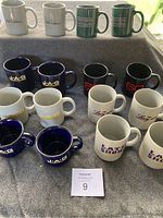 Multiple television show mugs arranged on a gray surface, showing different logos and colors including white, blue, green, and black mugs.