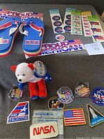 Overview photo showing USA sandals, plush bear, patches, 9-11 buttons, and stickers laid out on a dark cloth surface.