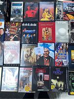 Top-down photo showing a collection of VHS tapes and DVDs arranged in a grid, including titles such as The Godfather, The Exorcist, Bruce Lee: Return of the Dragon, Ocean's 11, Moulin Rouge, History of the World, Lord of the Rings and others.