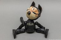 Image showing front view of the wooden Felix the Cat doll sitting with rope-linked legs and worn paint on the head and torso.