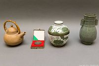Overview photo of all four items: teapot, medallion in case, floral glazed canister, and green vase.