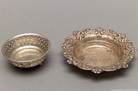 Two small sterling silver bowls side by side, showing size comparison and detailing of the repousse edge on the larger bowl and lattice design on the smaller bowl.