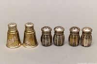 Three pairs of sterling silver salt and pepper shakers shown side by side on neutral gray background, showing size and design differences.