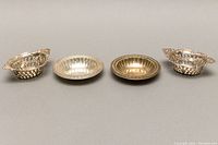 Photo showing four small sterling silver serving bowls arranged side by side on a flat surface, two oval reticulated ornate bowls on each end, two round scalloped edge bowls in center.