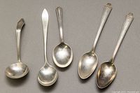 Five sterling silver spoons arranged on flat surface showing full length and handle details.